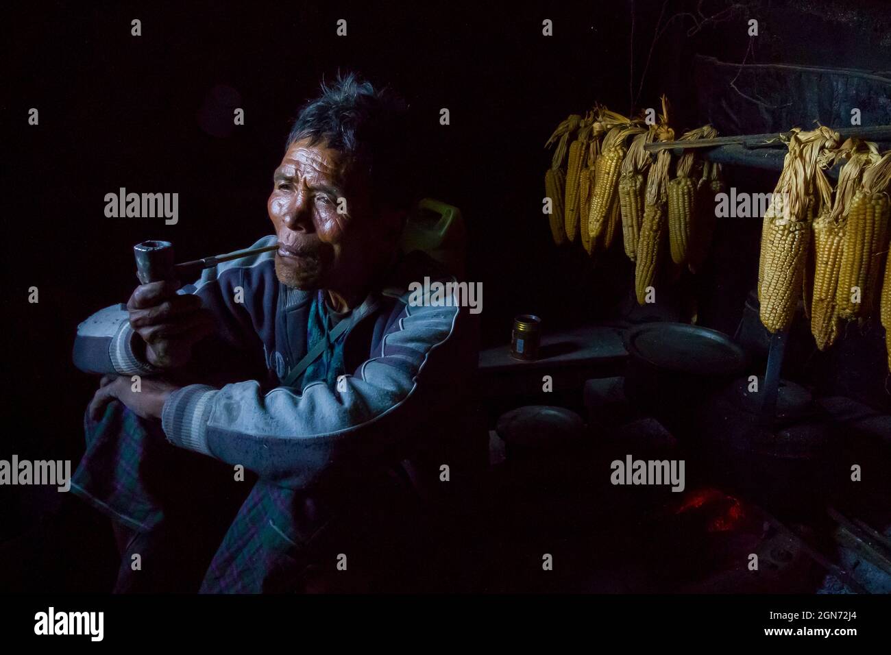 Un cacciatore nazionale Chin in pensionato seduto accanto alla sua cucina e fumando tubo. Foto Stock