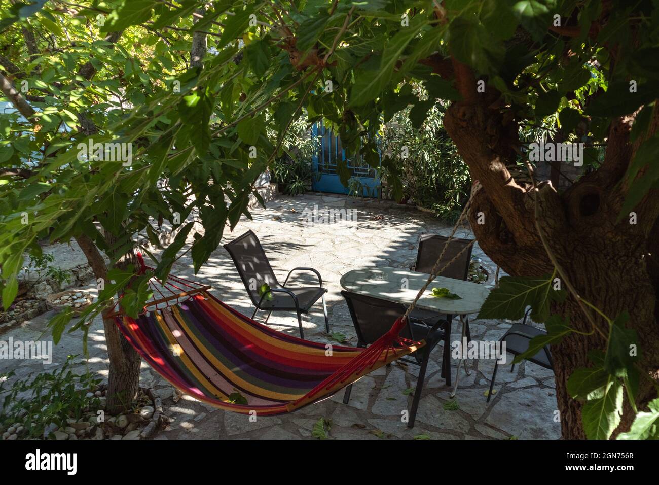 Amaca colorata e zona di ricreazione con il sole che splende attraverso rami di albero verde, tempo di ricreazione estate nel tradizionale cortile greco casa con pietra d Foto Stock