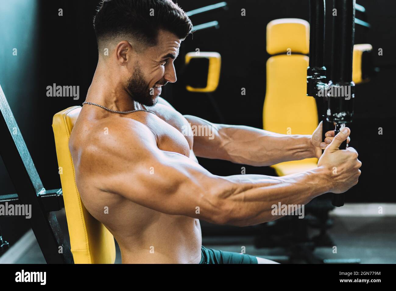 Profilo di un uomo che esercita con pesi usando una macchina in una palestra Foto Stock