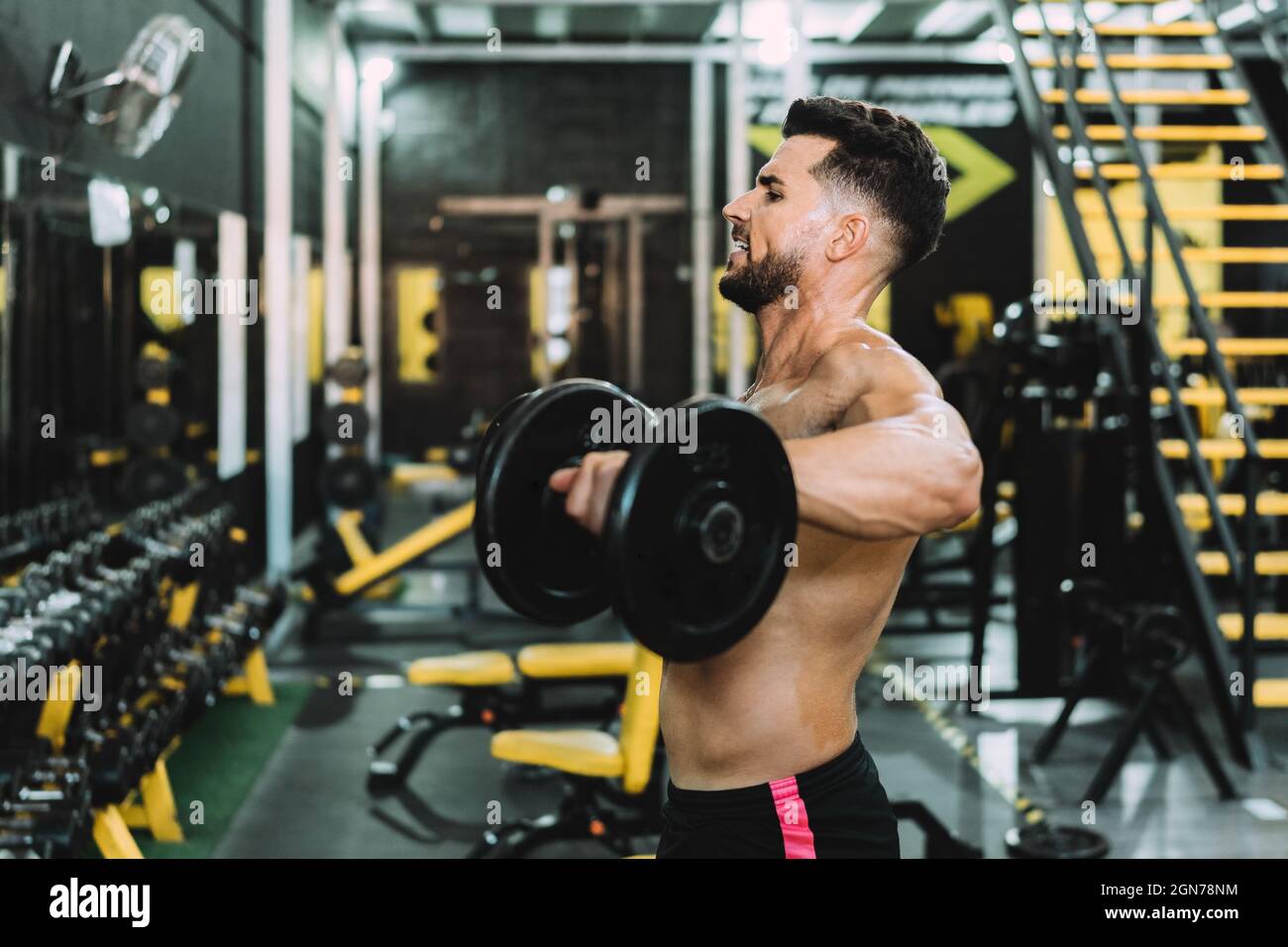 Uomo con espressione stanca facendo esercizi con peso in palestra Foto Stock