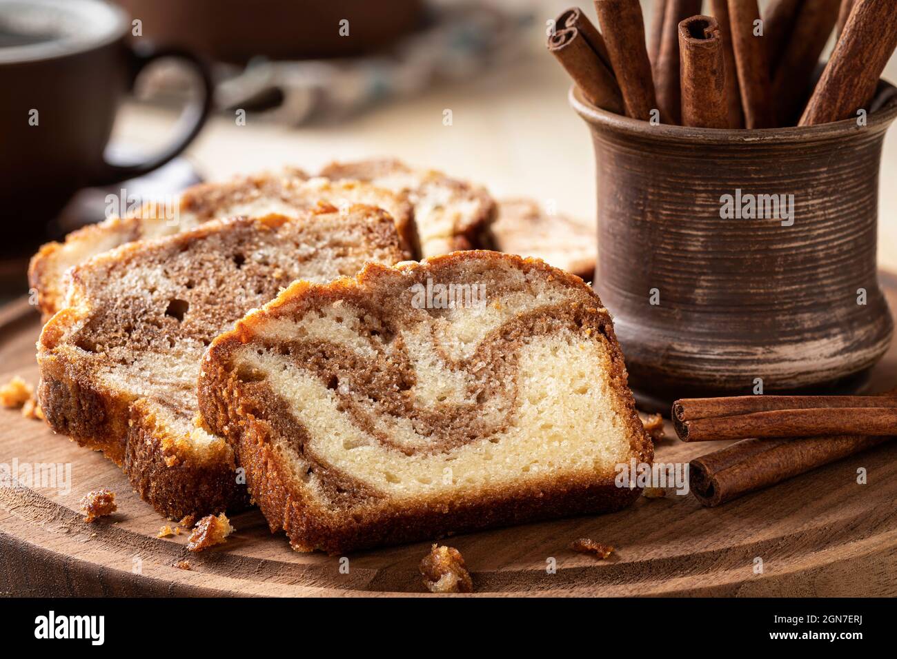 Primo piano di torta di pagnotta alla cannella a fette e bastoncini di cannella su un piatto di legno Foto Stock