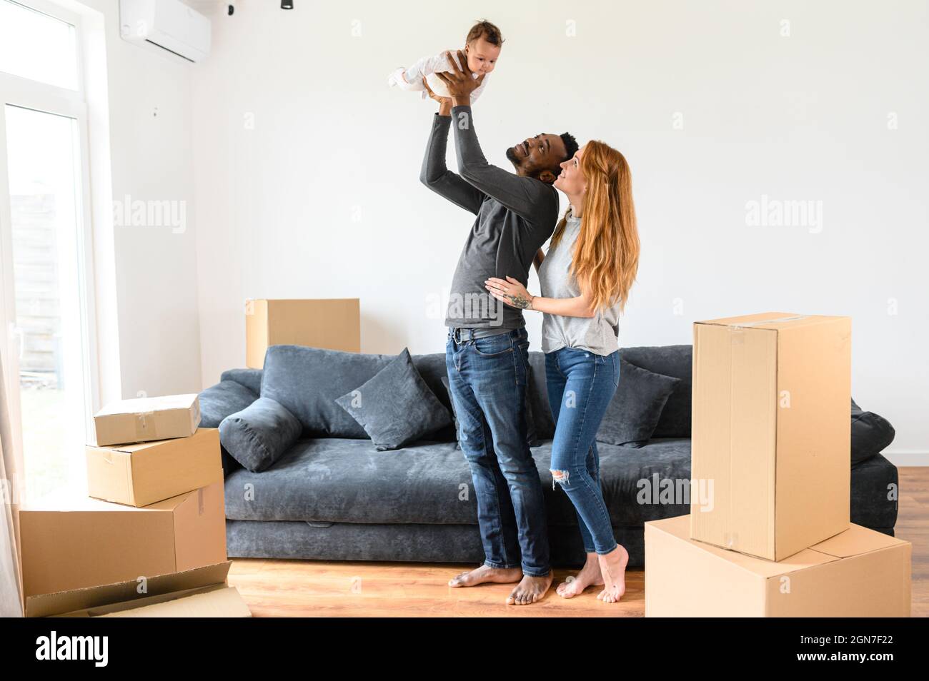 Felice famiglia misto-corsa si è riallocato in nuova casa, afro-americano marito e moglie caucasica in piedi con una figlia biraciale carino circondato scatole di cartone Foto Stock