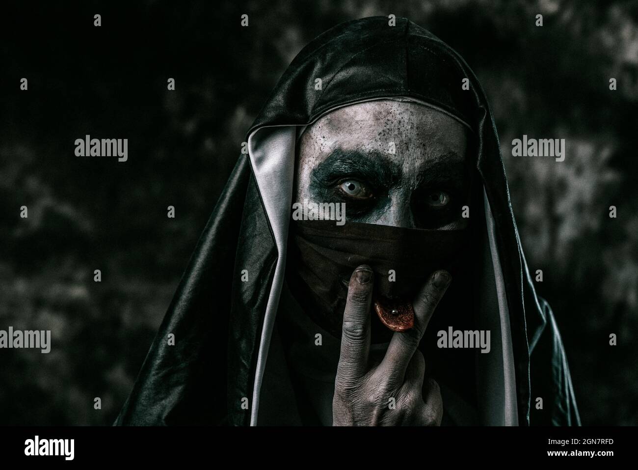 una monaca malvagia spaventosa, in una tipica abitudine bianca e nera, attacca la sua lingua traforata attraverso un foro nella sua maschera nera Foto Stock