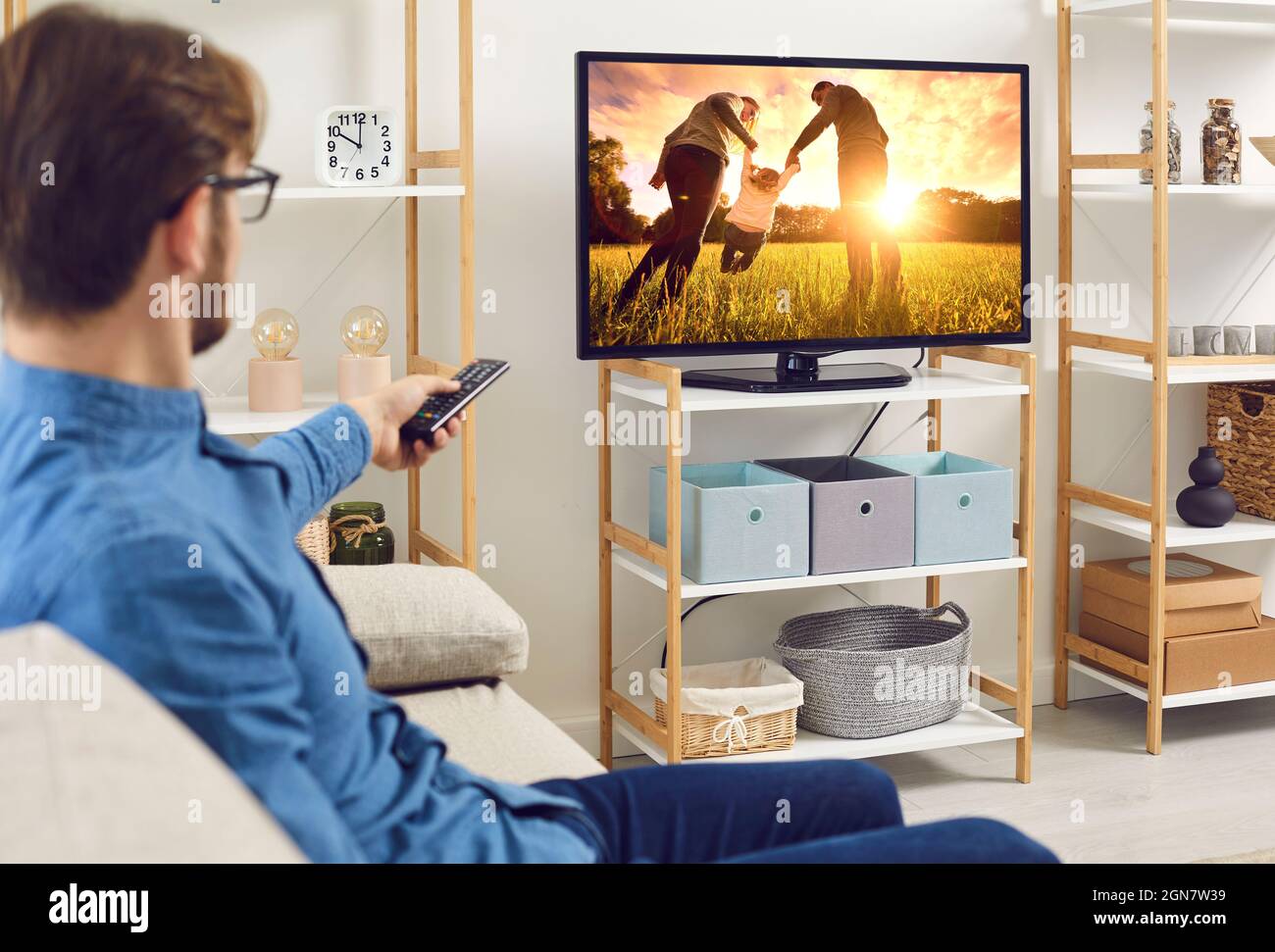 Uomo rilassato seduto su un divano a casa e guardando un film su un grande schermo TV Foto Stock