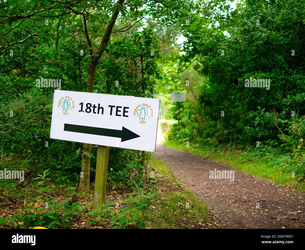 Un cartello bianco in un'area boschiva in un club di golf punta una grande freccia nera in direzione della diciottesima Tee, l'ultima buca sul campo da golf. Foto Stock