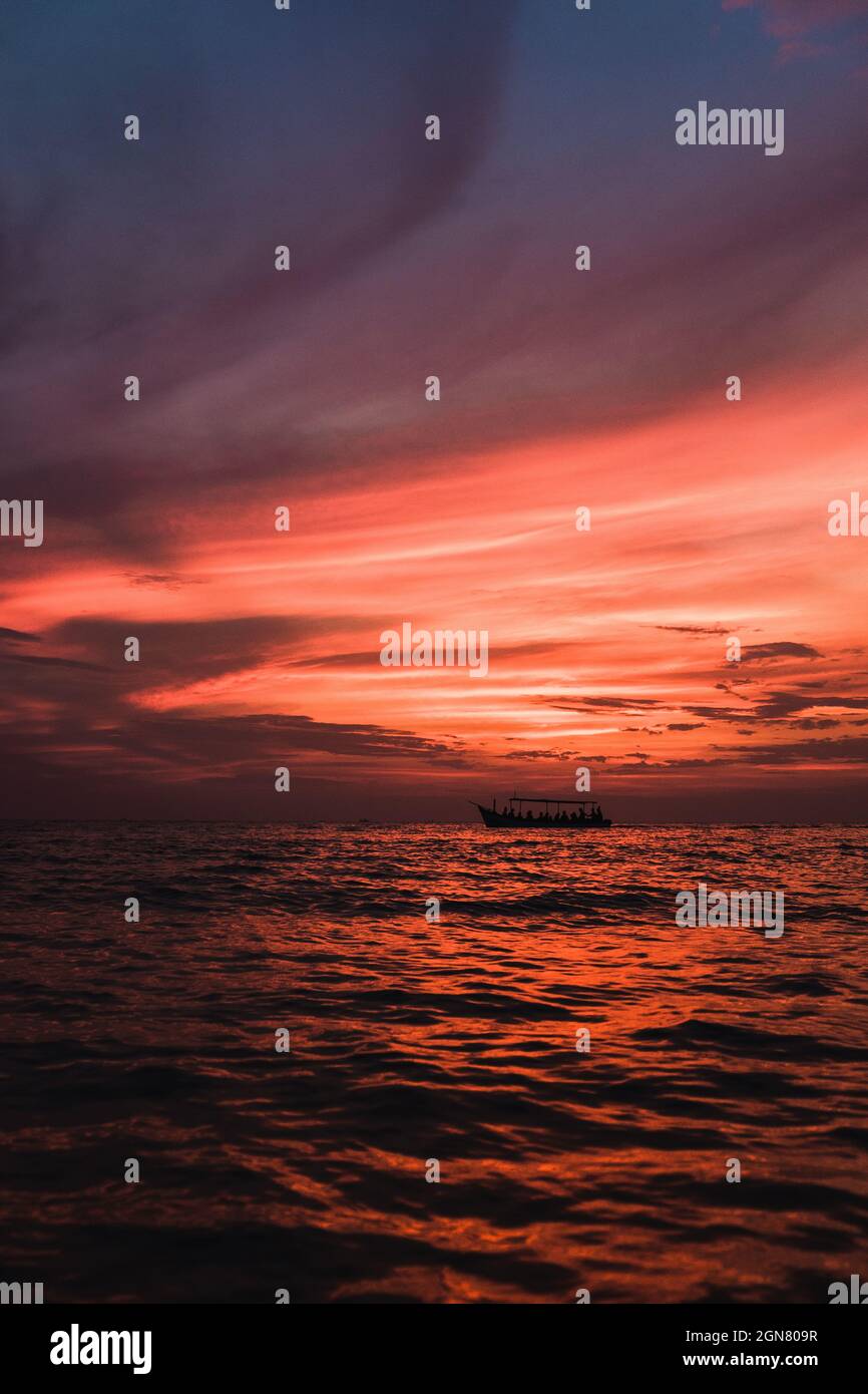 Vista panoramica sul mare al tramonto scarlatto. La barca naviga nell'oceano sullo sfondo di un tramonto rosso. Foto Stock