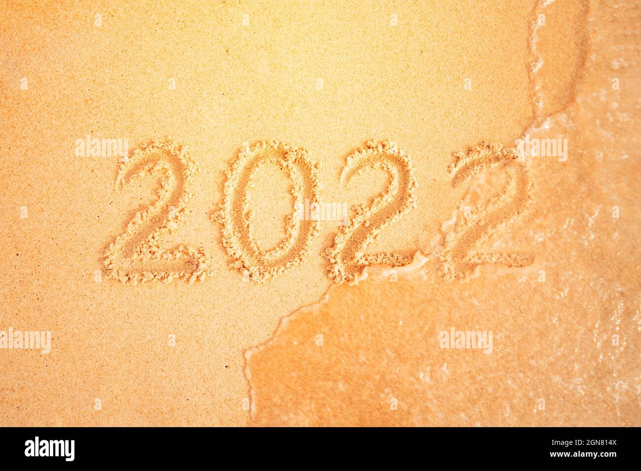 2022 scritto in sabbia, su spiaggia tropicale. Il concetto di cambiamento di anno. Onda di mare lava via l'iscrizione. Festa di capodanno in caldo co Foto Stock