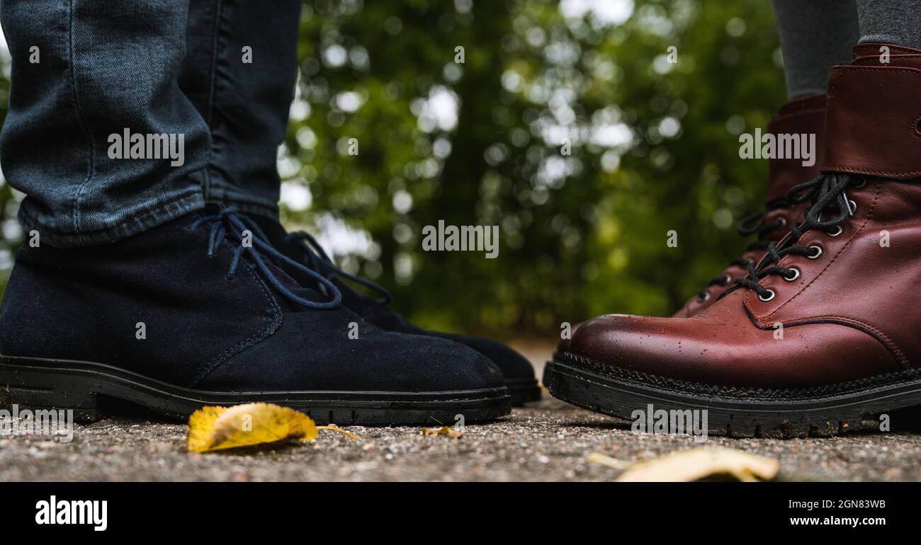 Piedi di coppia. L'uomo e la donna sono in piedi l'uno di fronte all'altro. Primo piano di scarpe in pelle scamosciata blu e stivali in pelle borgogna. Moda autunnale. Primo piano. Foto Stock