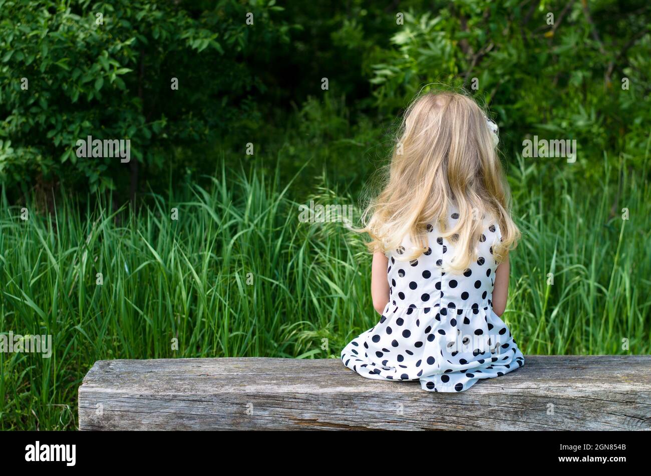 ragazza con lunghi capelli biondi seduta in panchina e in attesa Foto Stock
