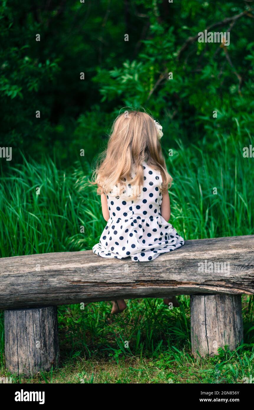 ragazza con lunghi capelli biondi seduta in panchina e in attesa Foto Stock