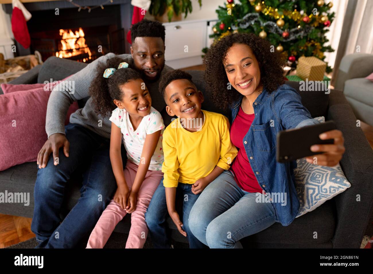 Felice famiglia afroamericana seduta sul divano e prendere selfie, decorazioni di natale in background. Famiglia natale tempo e festa insieme a. Foto Stock