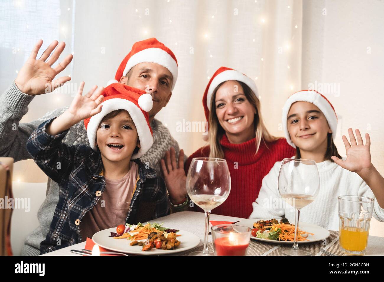 Ritratto di famiglia felice guardando la macchina fotografica durante la cena vegana festa di Natale con cappelli Babbo Natale - Focus su piccolo figlio Foto Stock