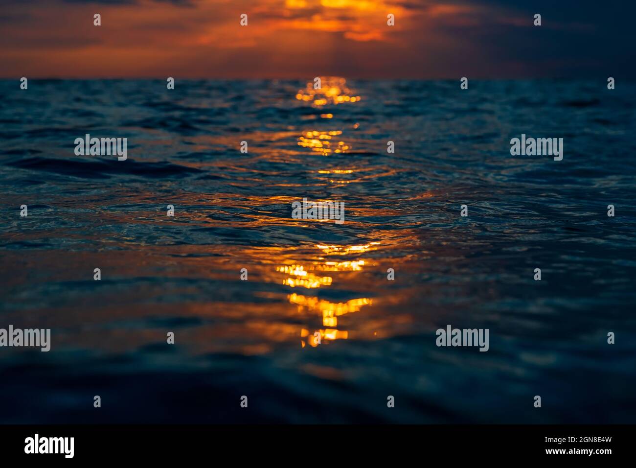 Tramonto nuvoloso con colori caldi e superficie dell'oceano con riflessi. Foto Stock