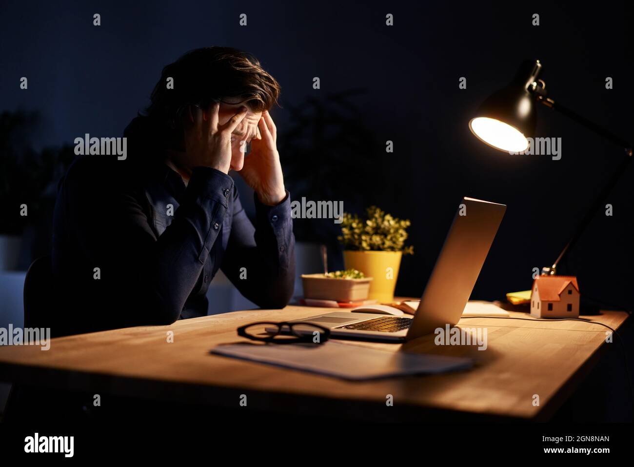Uomo d'affari stanco seduto alla scrivania mentre lavora a casa a tarda notte Foto Stock