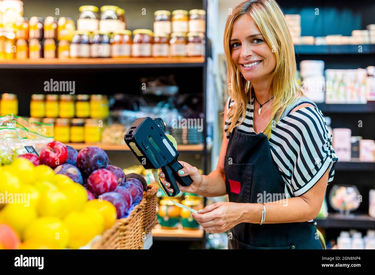 Donna di vendita matura che etichetta frutta in negozio biologico Foto Stock