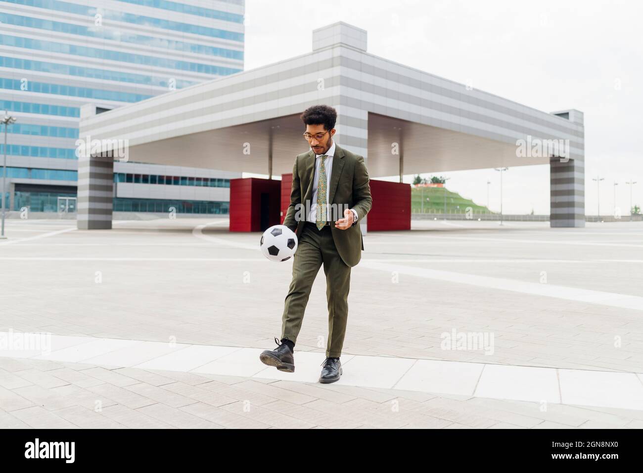 Uomo d'affari che calcia la palla di calcio mentre gioca sul sentiero Foto Stock