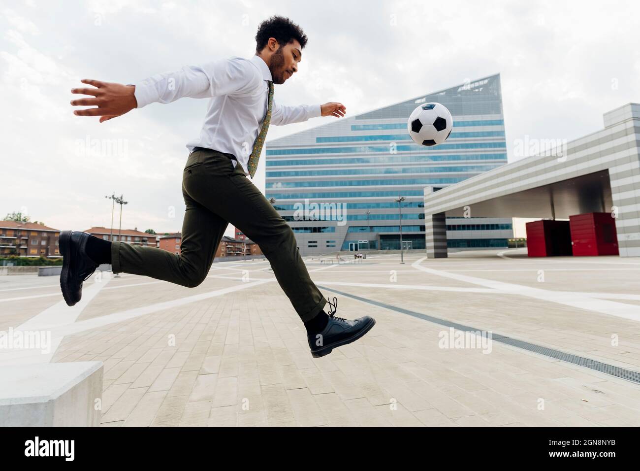 Uomo d'affari che gioca con la palla di calcio in città Foto Stock