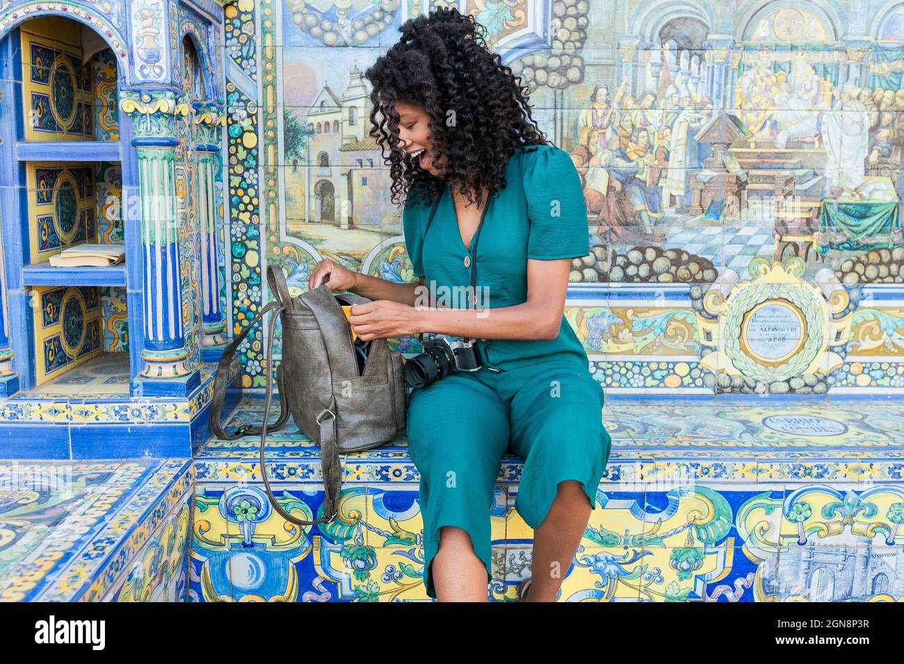 Sorprende lo zaino di apertura femminile mentre si siede di fronte al mosaico a Plaza De Espana, Siviglia, Spagna Foto Stock