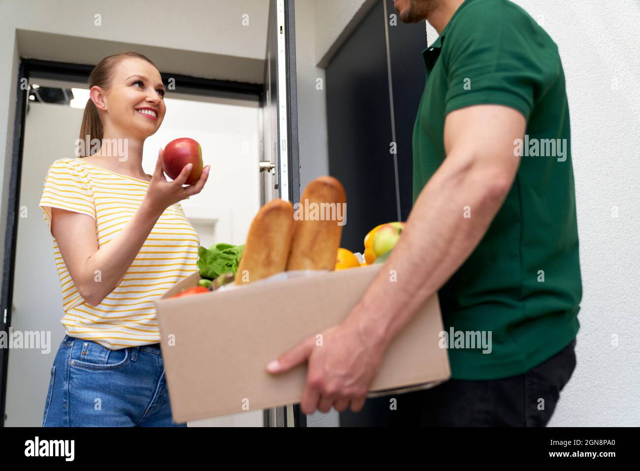 Cliente femmina che controlla la frutta mentre riceve l'ordine dal consegnatore alla porta Foto Stock