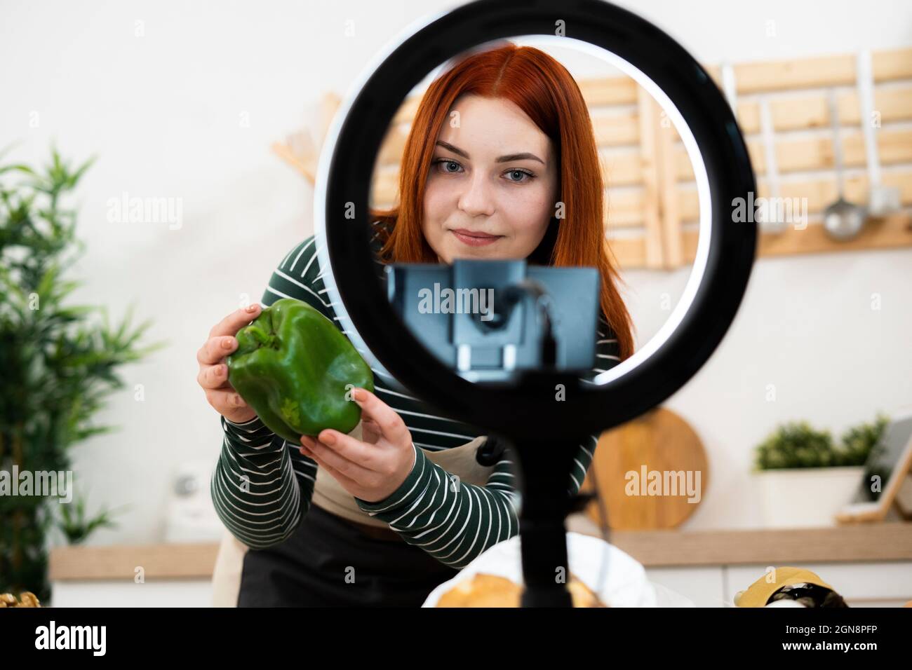 Influencer femminile che mostra peperone verde mentre filma attraverso il telefono cellulare a casa Foto Stock