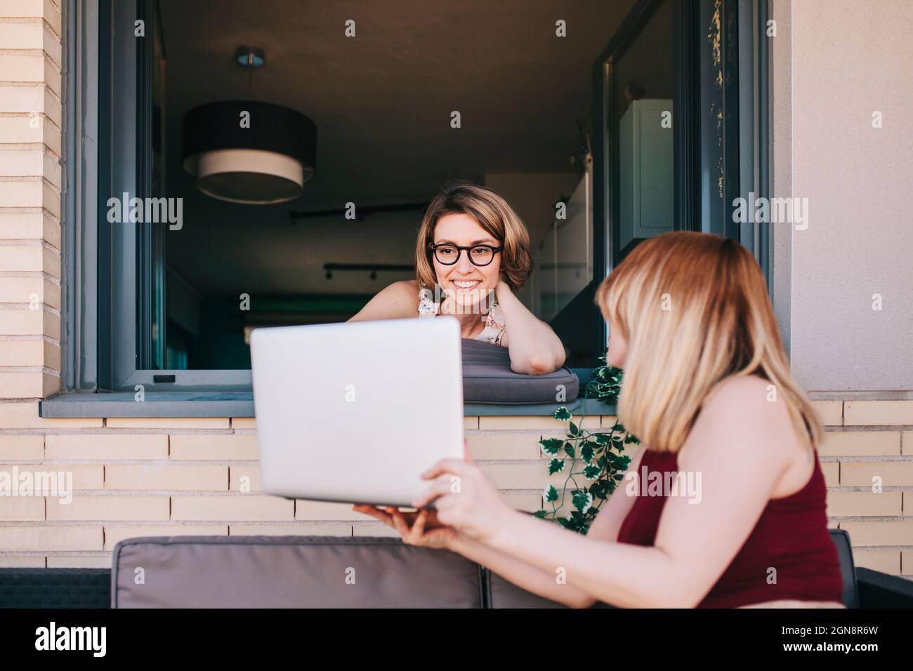 Donna d'affari che mostra il laptop al collega che si appoggia sulla finestra Foto Stock