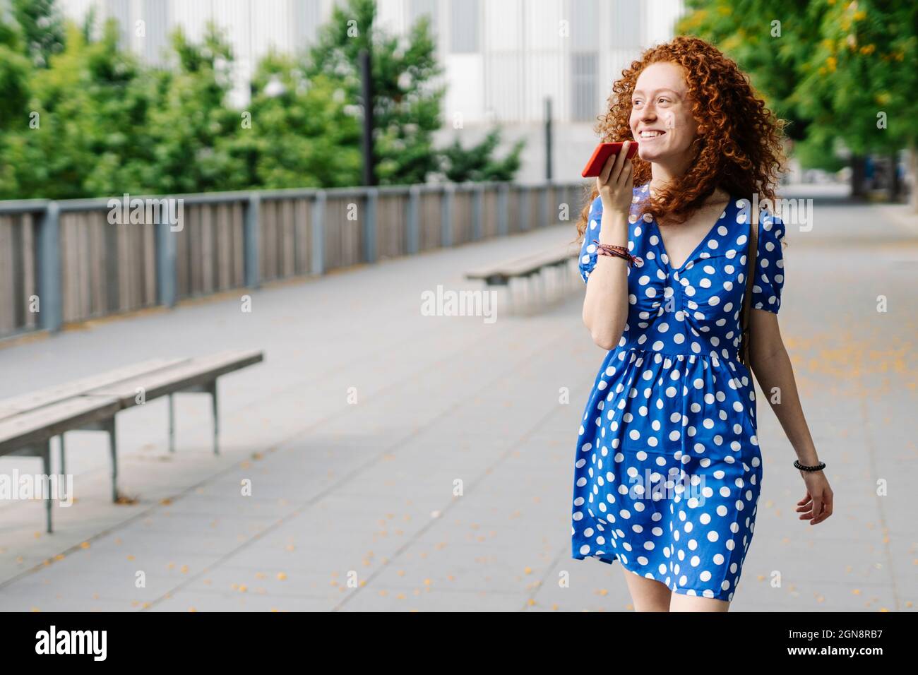 Donna sorridente che invia messaggi vocali tramite telefono cellulare mentre cammina sul sentiero Foto Stock