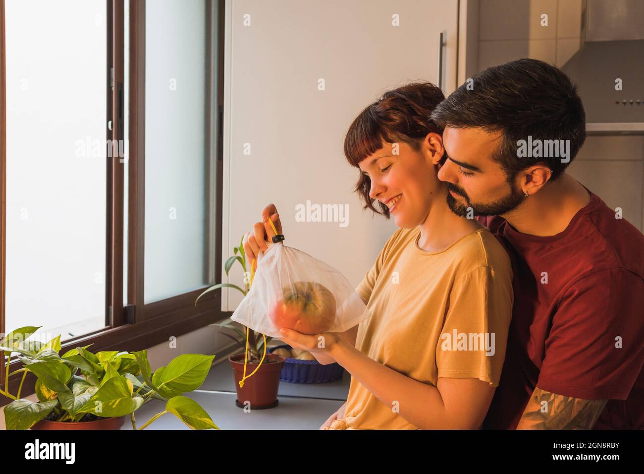 Uomo che abbraccia la ragazza che tiene il pomodoro beefsteak in cucina a casa Foto Stock