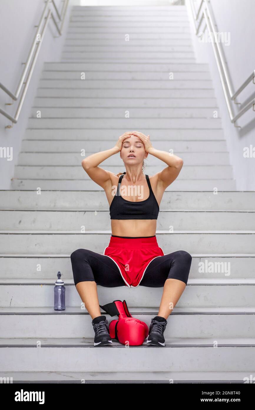 Boxer femminile con testa in mani seduta su scala Foto Stock