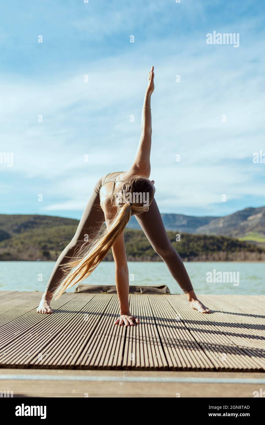 Donna attiva che fa il triangolo posa sul jetty Foto Stock