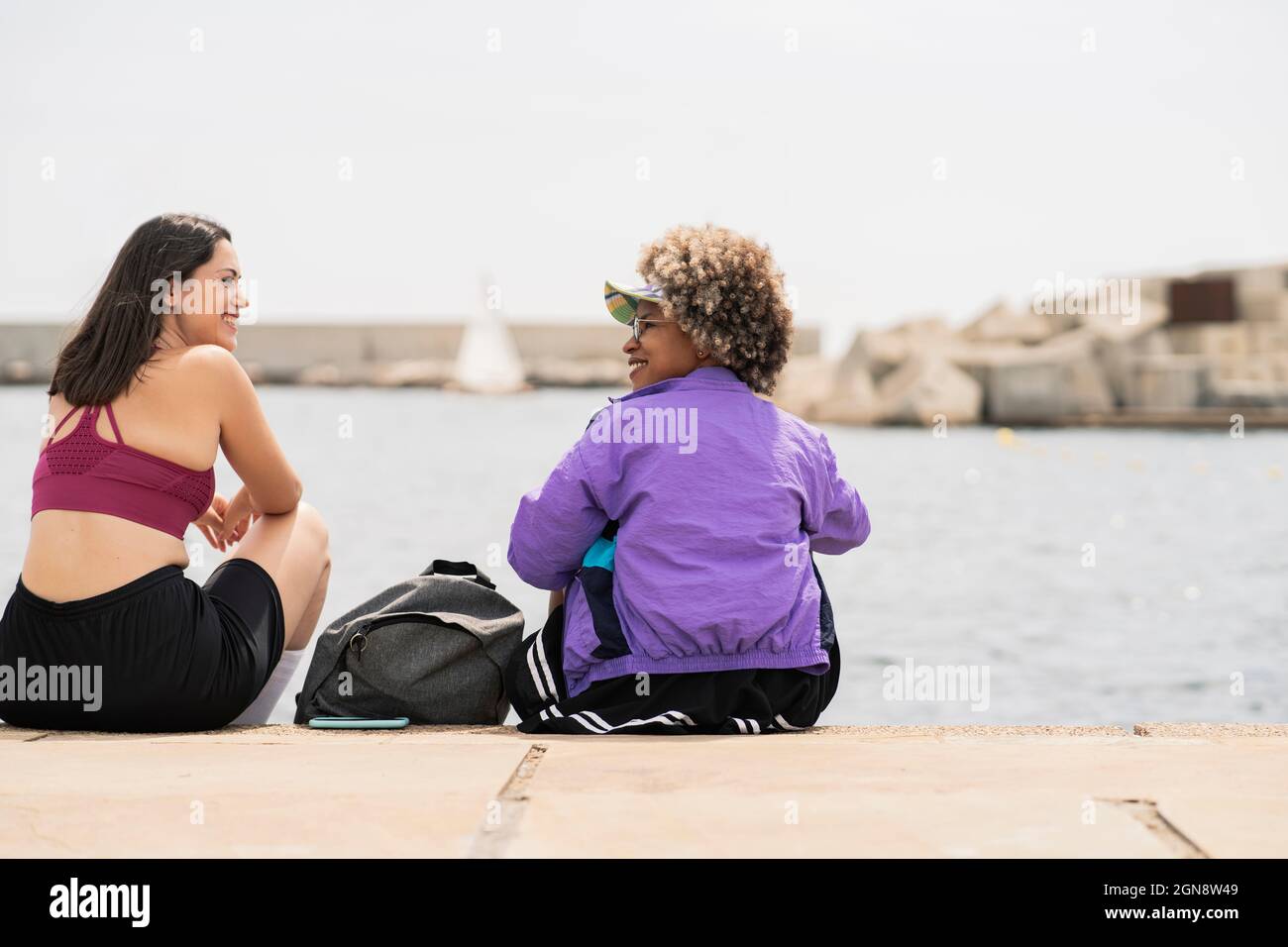 Sorridenti donne adulte che si guardano mentre si siedono sul lungomare Foto Stock