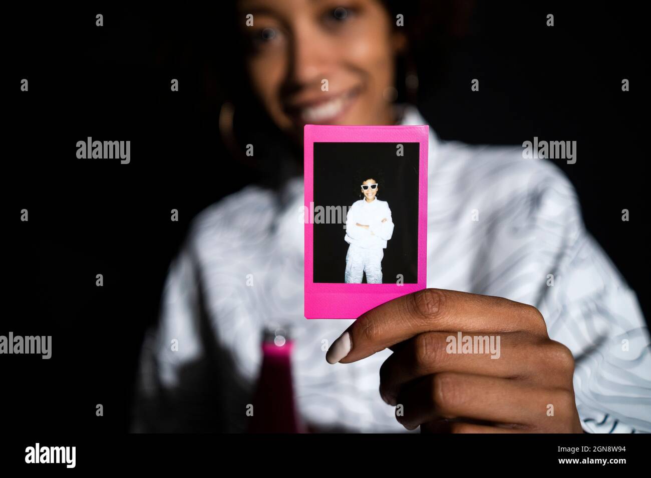 Donna che mostra fotografia polaroid su sfondo nero Foto Stock