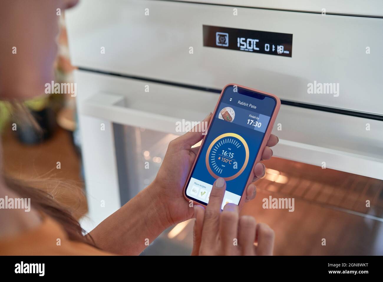 Donna che regola la temperatura del forno su smartphone in casa moderna Foto Stock