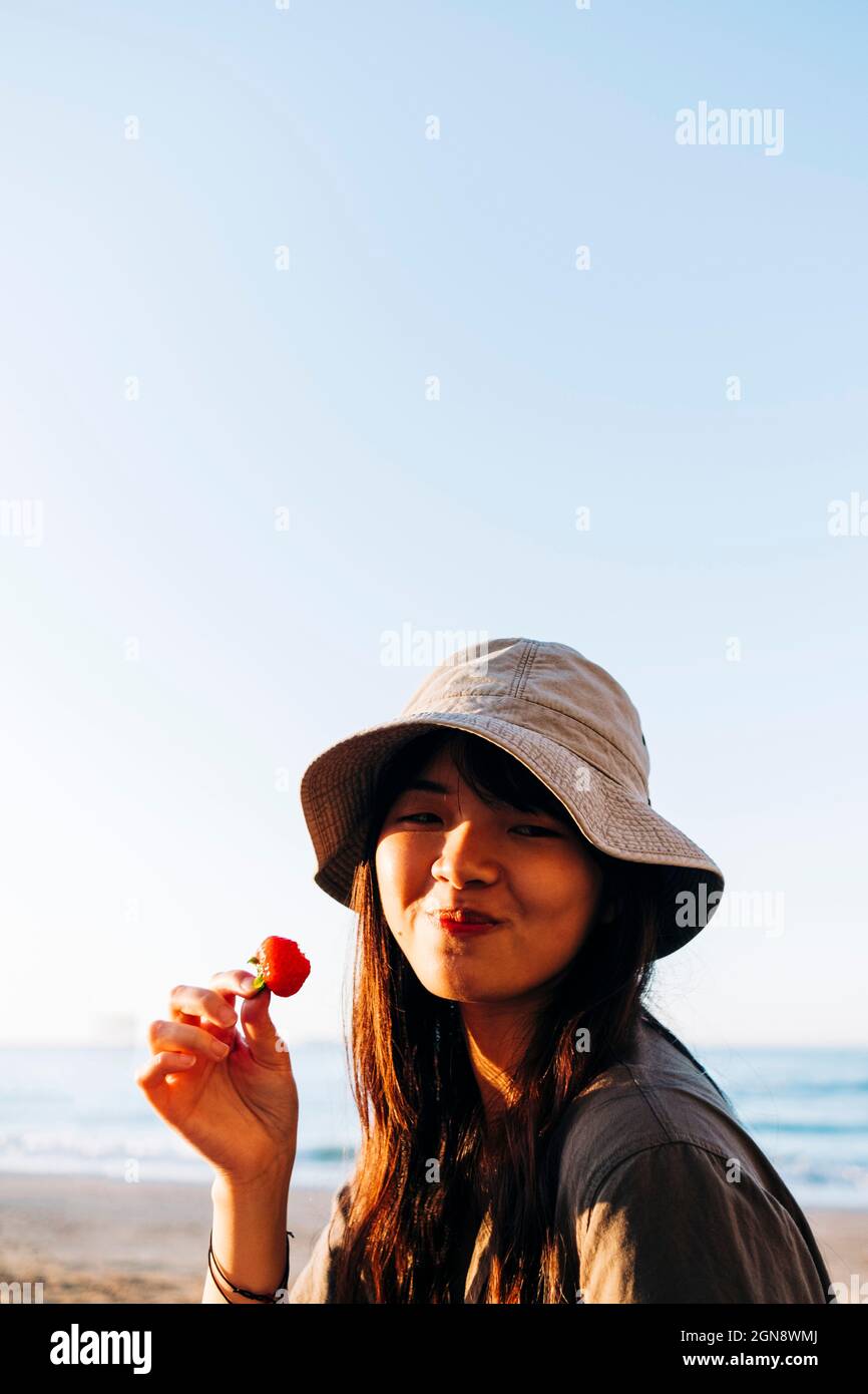 Bella giovane donna che mangia fragole in spiaggia Foto Stock