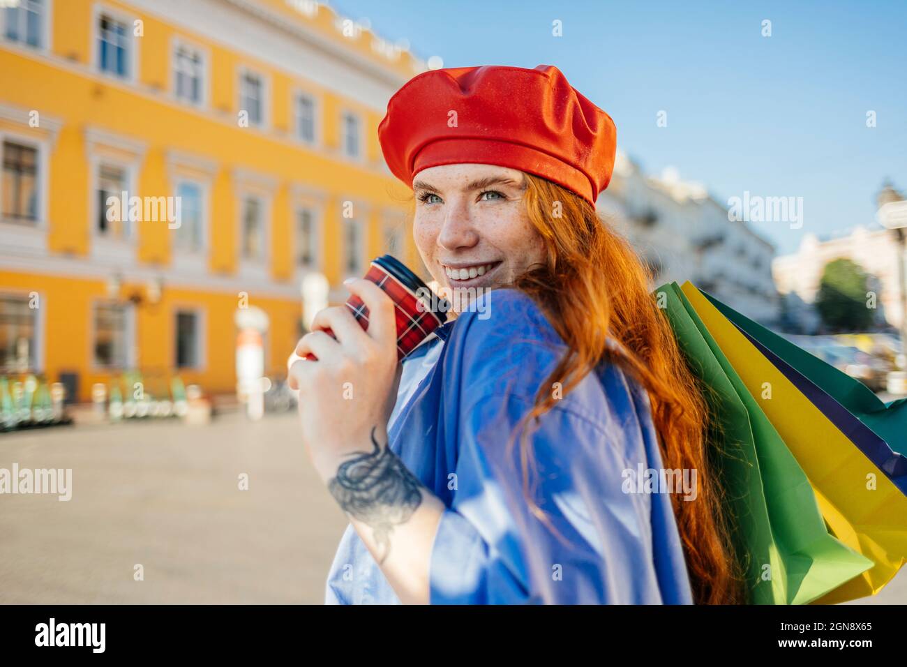 Giovane donna che ha il caffè mentre tiene i sacchetti della spesa Foto Stock