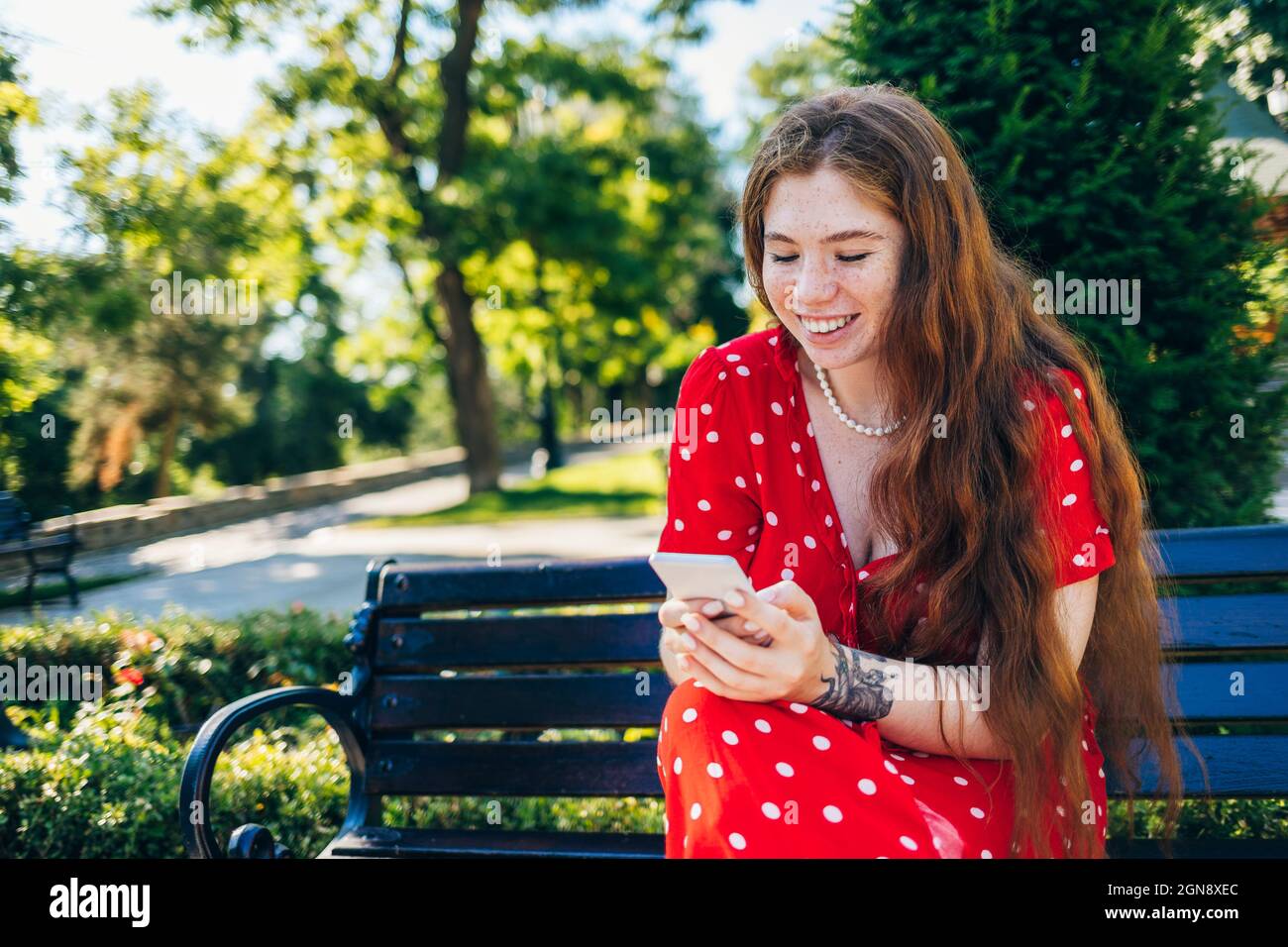 Donna felice utilizzando il telefono cellulare mentre si siede sulla panca Foto Stock