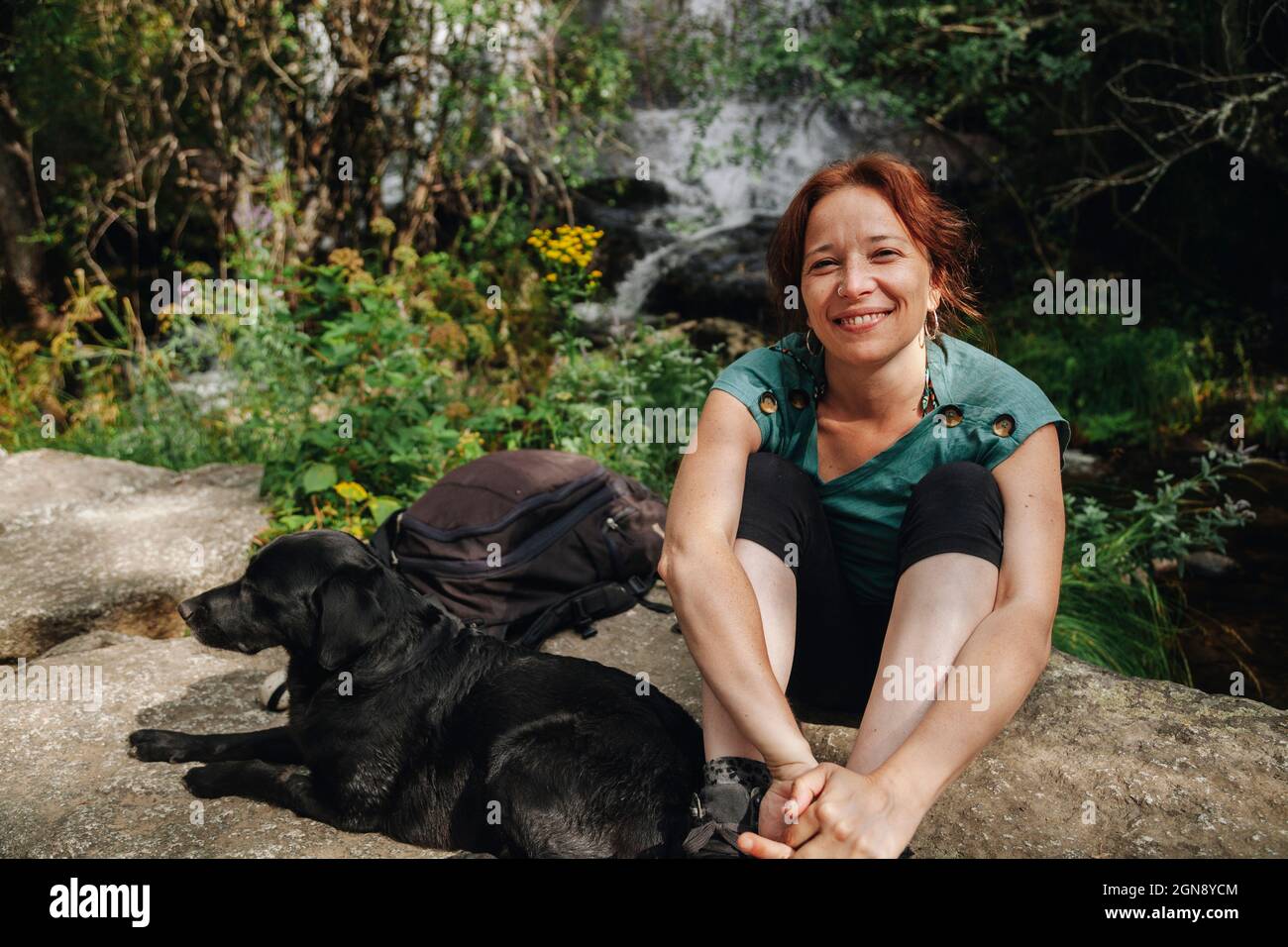 Sorridente donna adulta proprietario seduto accanto al cane nella foresta Foto Stock