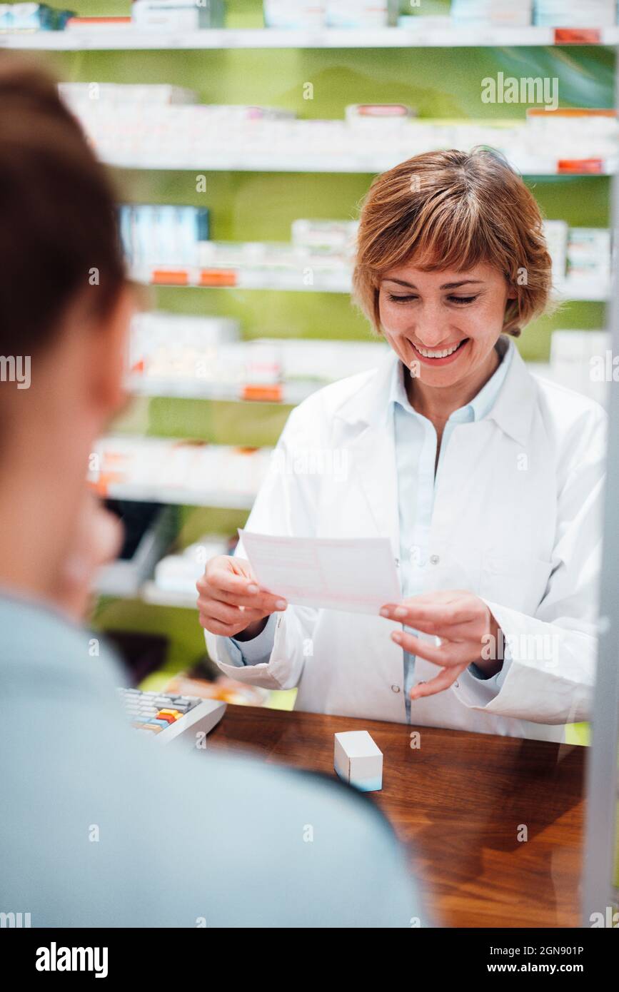 Il farmacista sorridente legge la prescrizione mentre si trova in piedi con il cliente in negozio Foto Stock