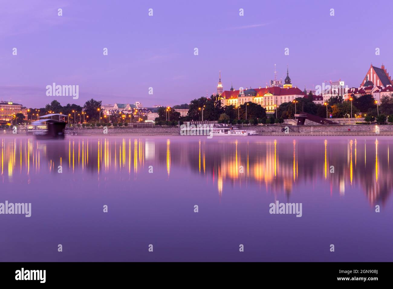 Illuminato il paesaggio della Città Vecchia di Varsavia con il Castello reale, la Cattedrale e gli edifici medievali, durante l'alba viola con riflessi nella calma Vistola Foto Stock
