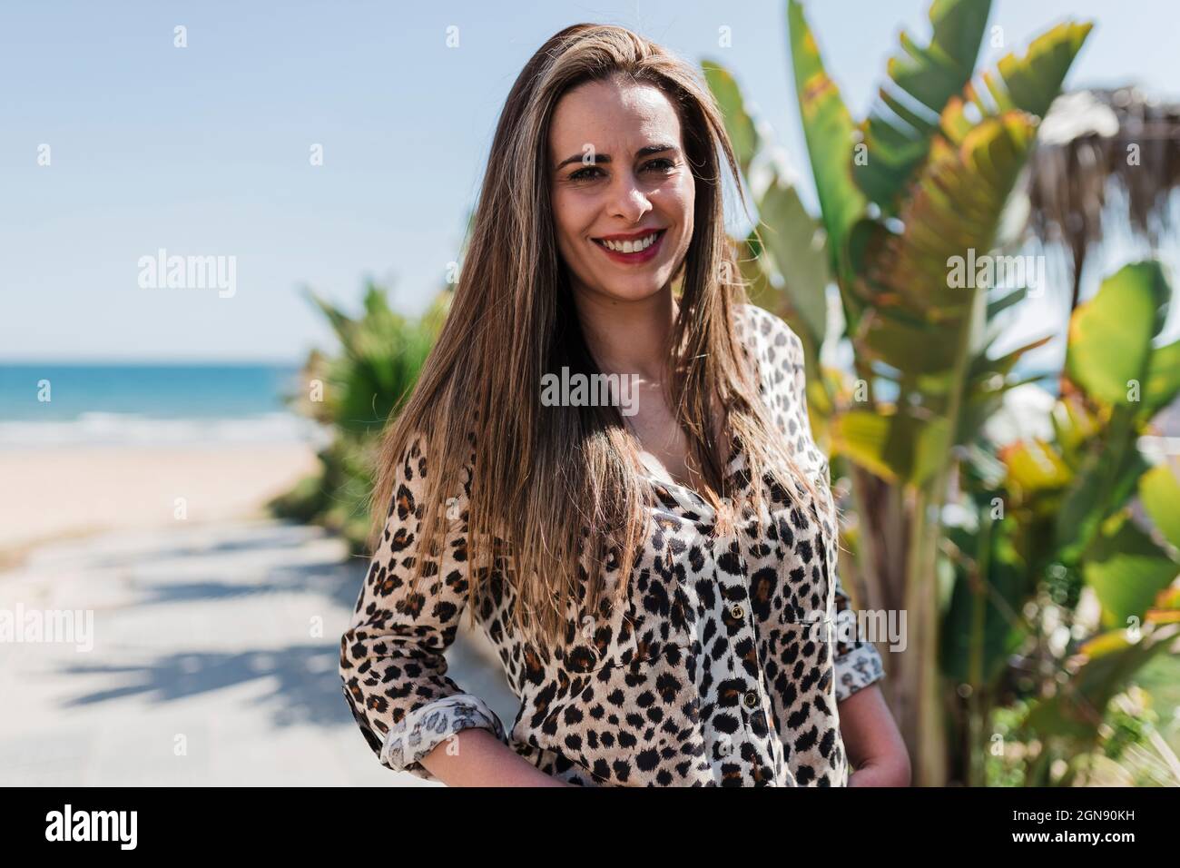 Donna sorridente che indossa una maglietta con stampa Cheetah in spiaggia il giorno di sole Foto Stock