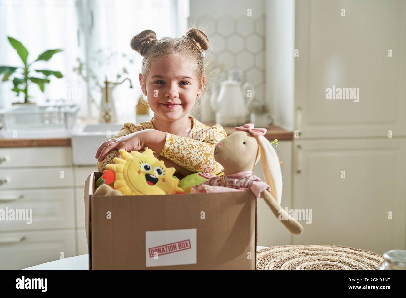 Ragazza sorridente appoggiata sulla scatola di donazione a casa Foto Stock