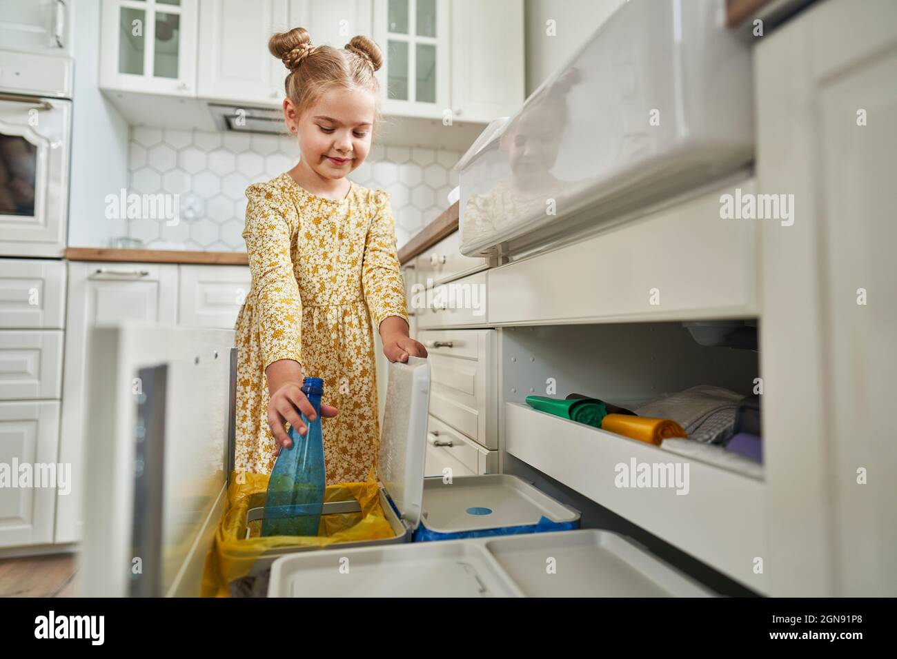 Ragazza con ciambelle di capelli gettando bottiglia di plastica nel cestino dei rifiuti Foto Stock