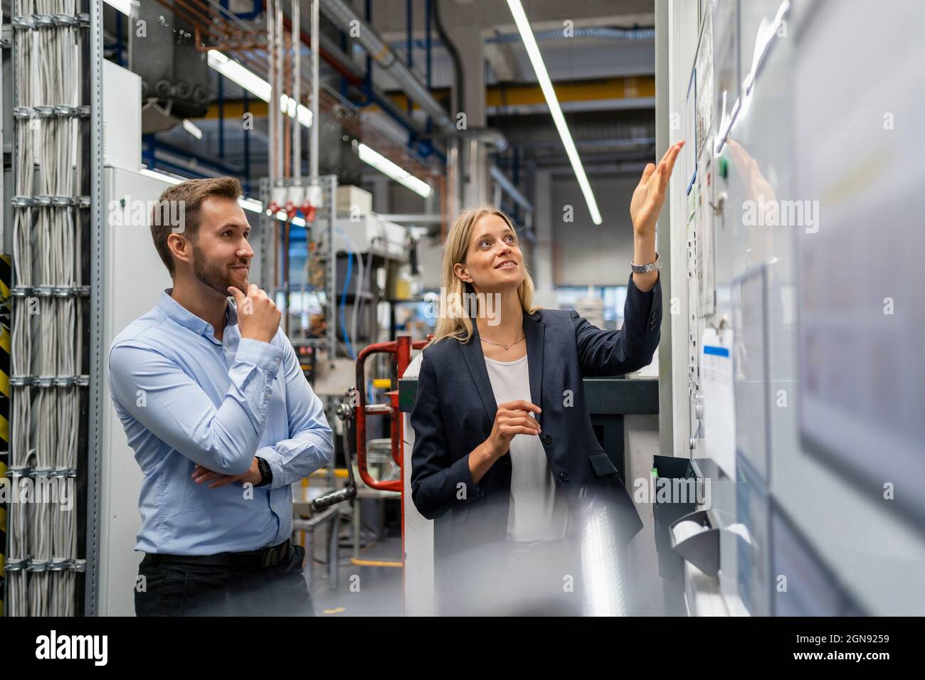 Donna d'affari che spiega il collega sulla lavagna in fabbrica Foto Stock