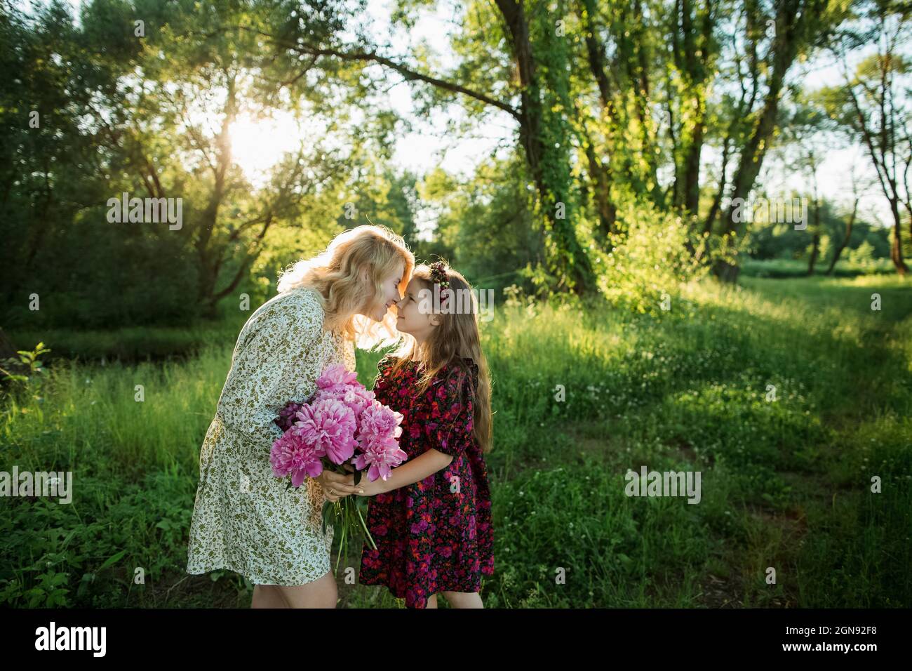 Mamma e figlia giocose che tengono fiori di peonia mentre strofinano i nasi Foto Stock