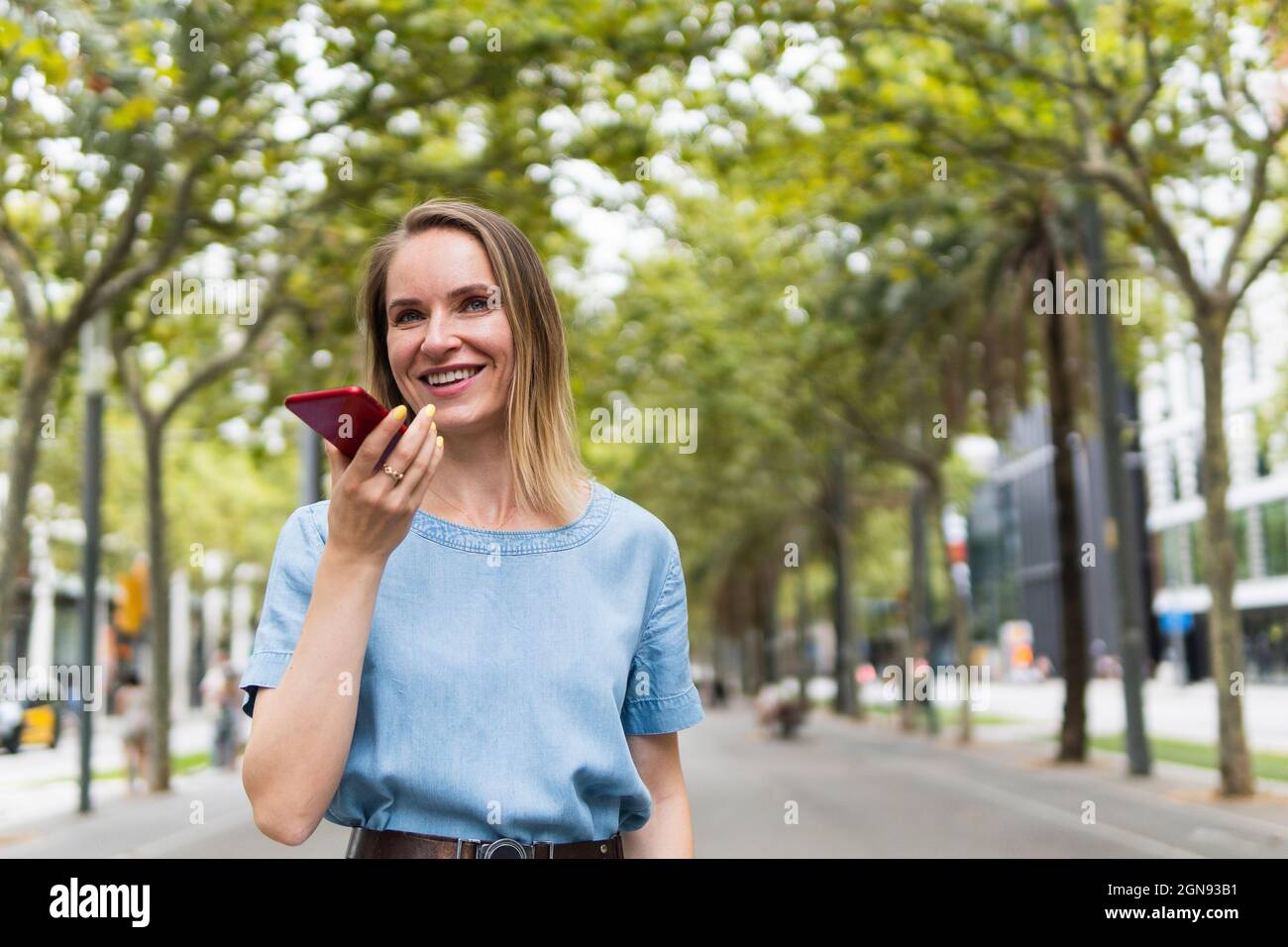 Felice ragazza bionda professionale che invia la segreteria tramite smartphone Foto Stock