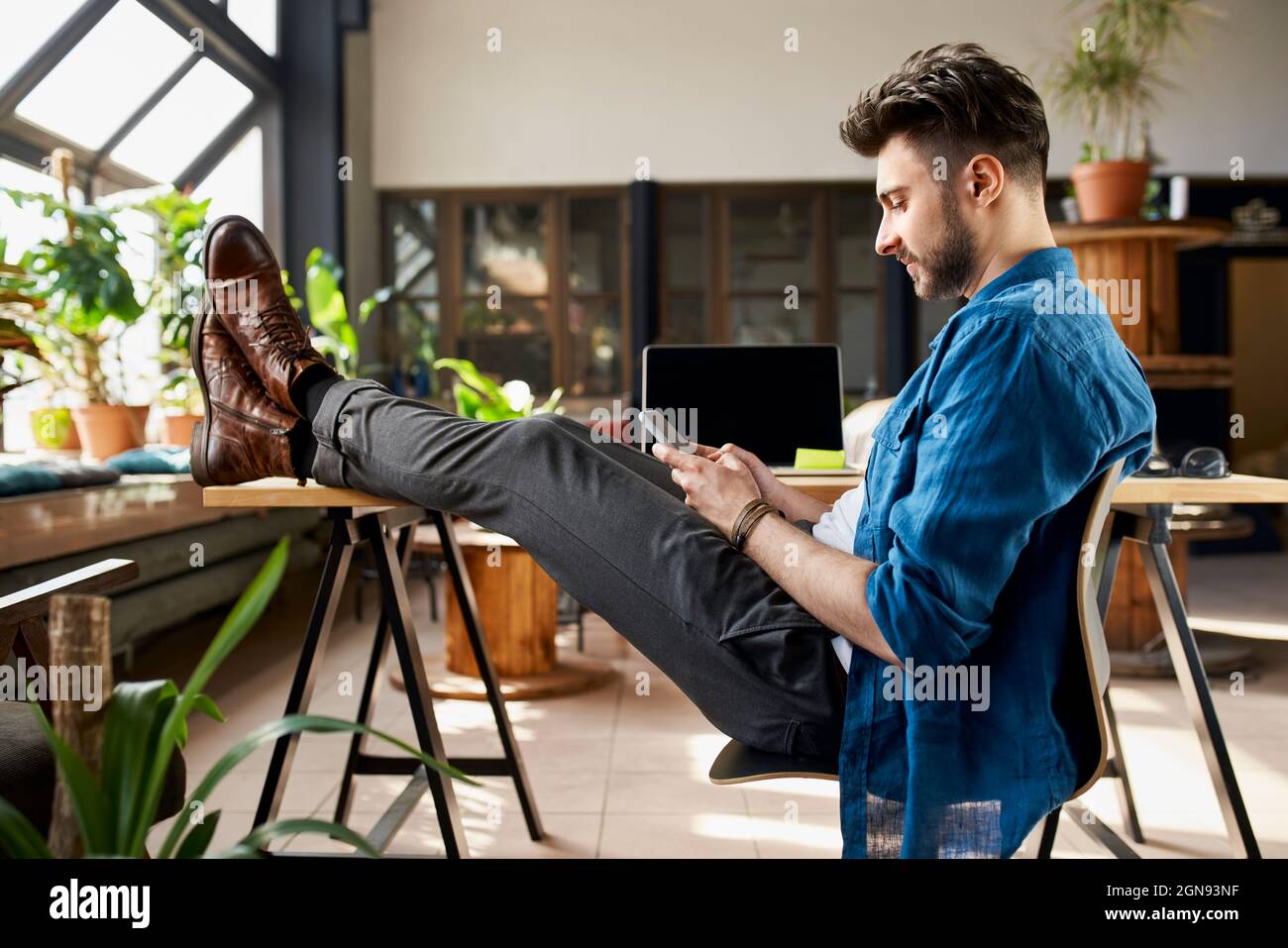Messaggi di testo uomo tramite telefono cellulare mentre si siede sulla sedia a casa Foto Stock
