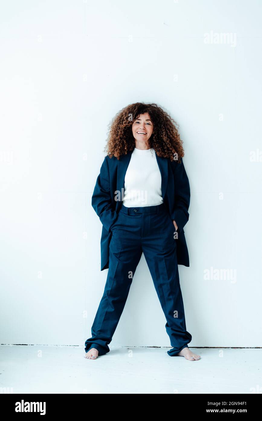 Donna d'affari matura con capelli ricci in piedi da parete grigia Foto Stock