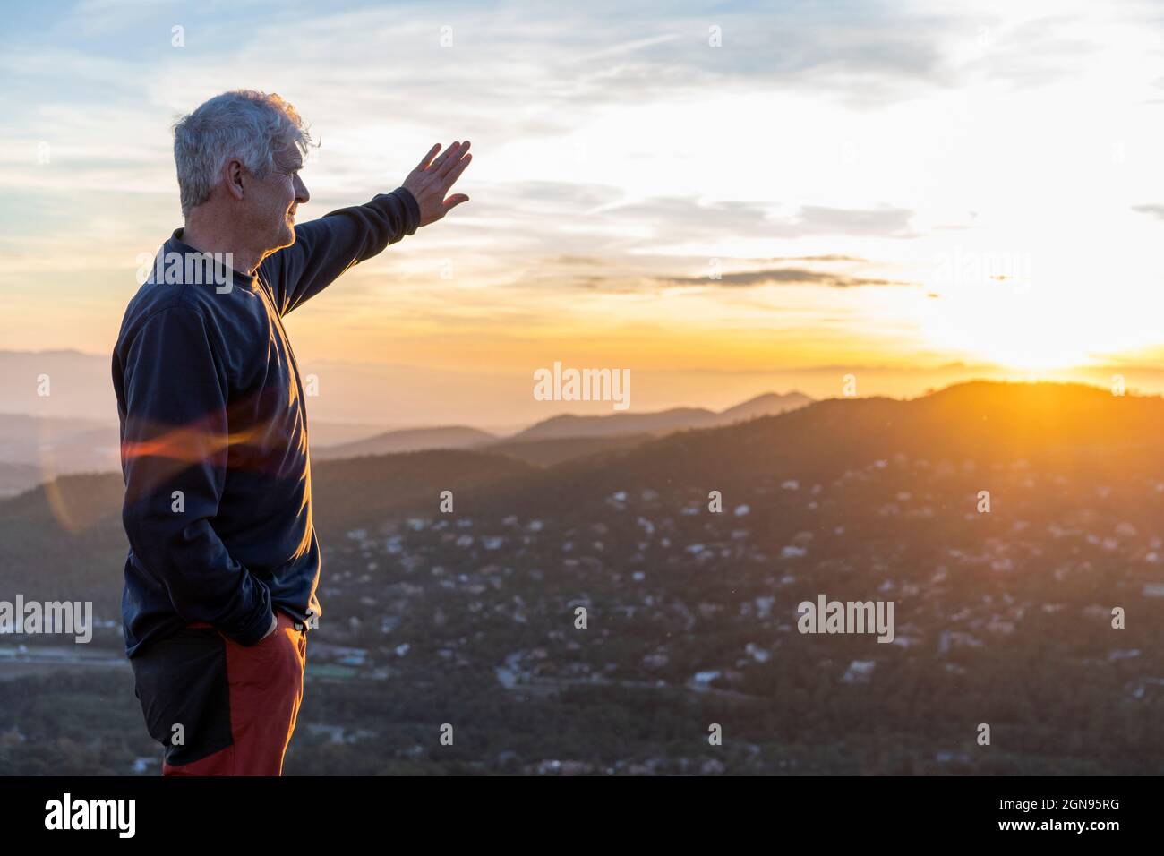 L'uomo anziano scherma gli occhi mentre si alza sulla montagna durante il tramonto Foto Stock