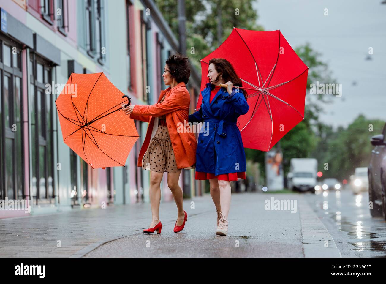 Donna sorridente che guarda un amico femmina che lotta con ombrello Foto Stock
