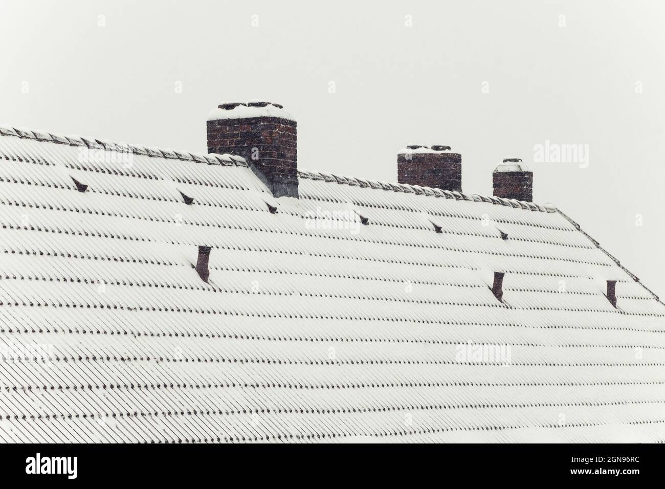 Tetto coperto di neve con tre camini e cielo bianco. Simbolo per le vacanze di natale e l'inverno Foto Stock