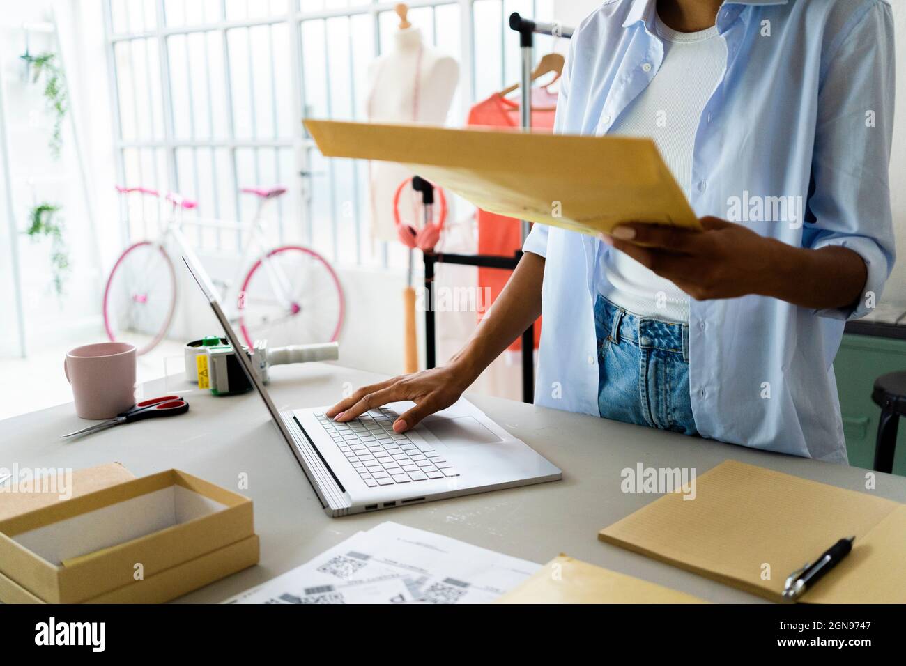 Stilista di moda femminile che utilizza un computer portatile mentre tiene il pacchetto in studio Foto Stock
